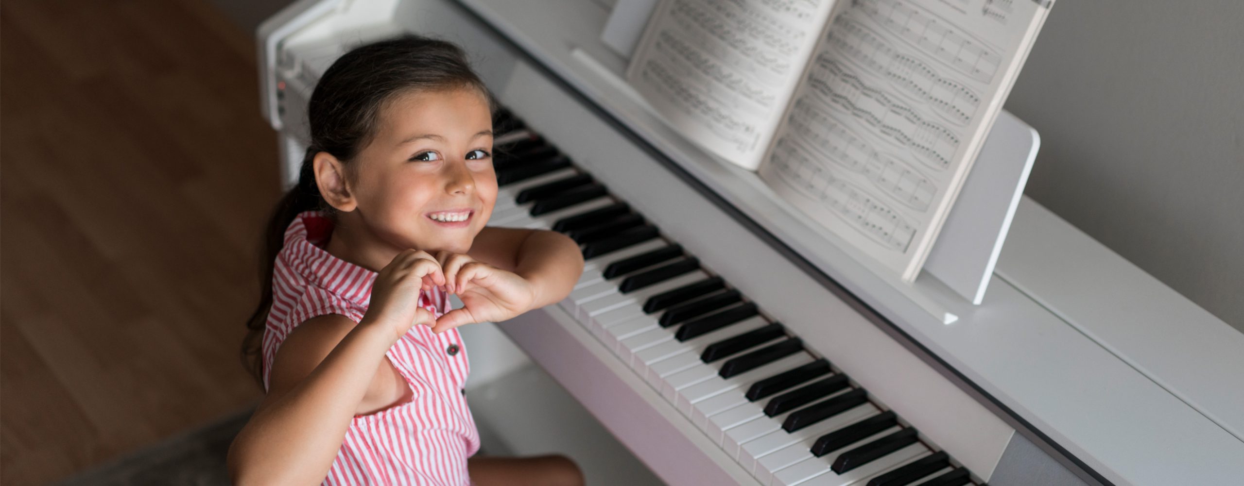 Young piano student smiling beside a white piano during practice at home